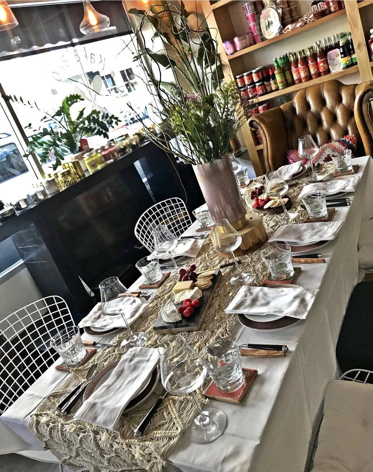 The Kaka'ako Market dining area set for an intimate gathering — white linens, wine glasses, a cheese board, and fresh flowers